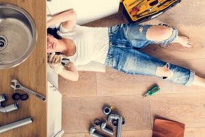 woman performing DIY repairs on kitchen sink plumbing problem