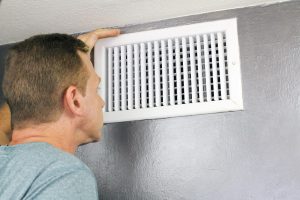 a man looks inside an air register and wonders how often he should have his ducts cleaned for better indoor air quality