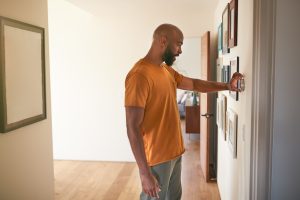 An African American man adjusts his thermostat after learning about the differences between heat pump vs. furnace.