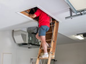 a man climbs a pull-down ladder in his garage to assess his attic insulation